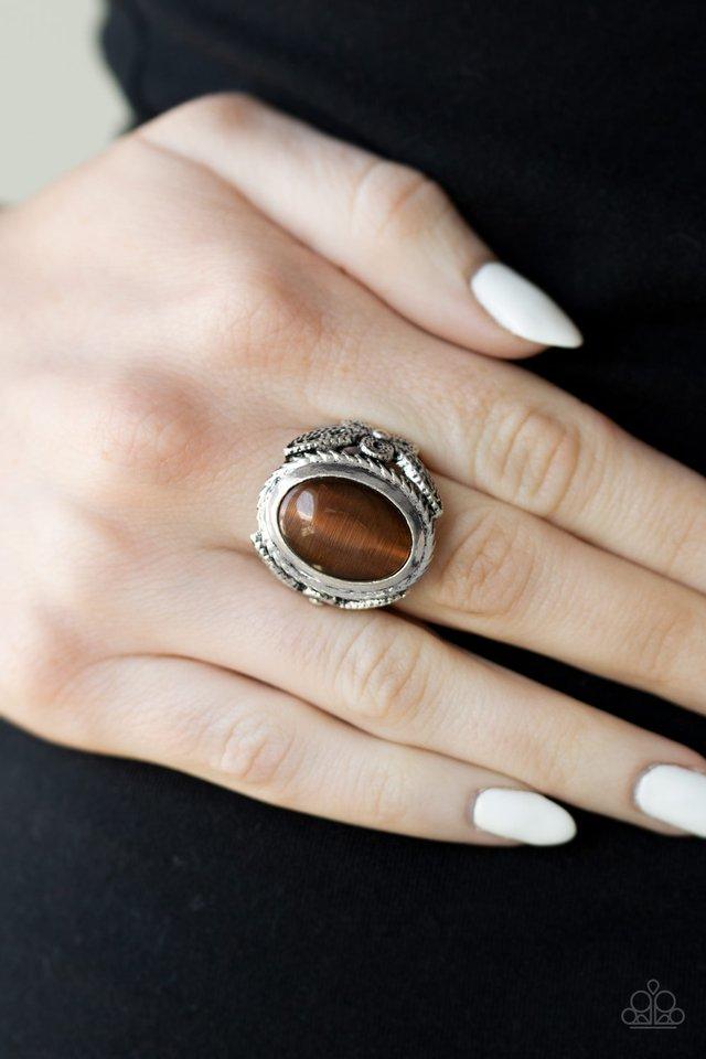 A brown cat's eye stone is pressed into the center of an ornate silver frame radiating with studded filigree for a whimsical flair. Features a stretchy band for a flexible fit.  Sold as one individual ring.