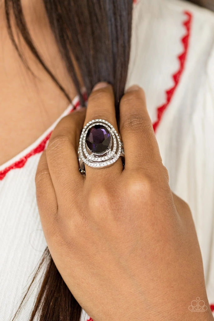 A glittery purple gem sits atop stacked silver frames radiating with glassy white rhinestones for a timeless look. Features a stretchy band for a flexible fit.  Sold as one individual ring.