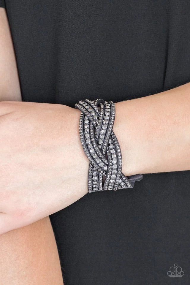 Varying in size, glittery hematite rhinestones are encrusted along interwoven gray suede bands, creating blinding shimmer across the wrist. Features an adjustable snap closure. Sold as one individual bracelet.