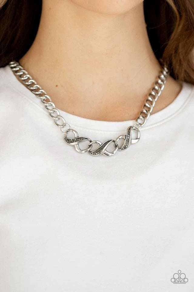Encrusted in sections of dainty hematite rhinestones, three interlinked silver infinity charms attach to an oversized silver chain below the collar for a bold industrial style. Features an adjustable clasp closure. Sold as one individual necklace. Includes one pair of matching earrings.