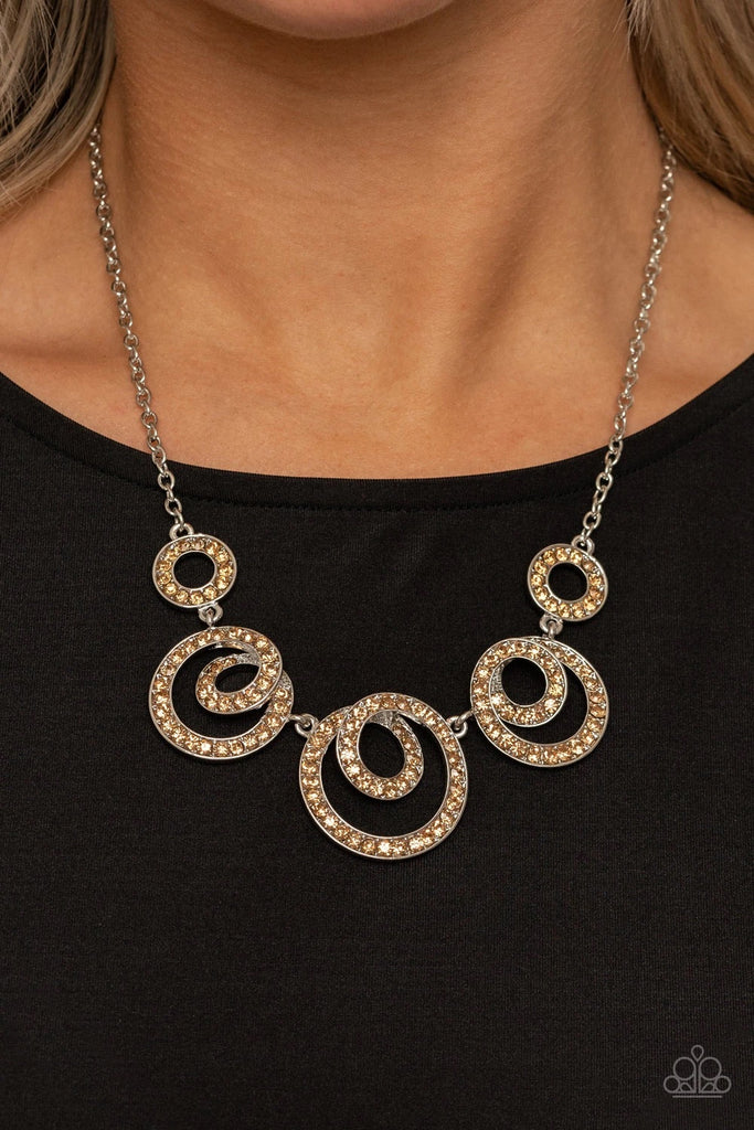 Encrusted in glassy topaz rhinestones, swirling silver frames delicately connect below the collar for a statement-making finish. Features an adjustable clasp closure.  Sold as one individual necklace. Includes one pair of matching earrings.