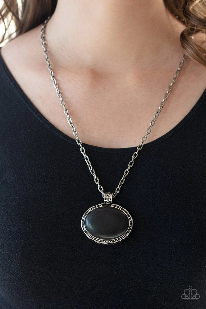 Chiseled into a smooth oval, an oversized black stone is pressed into a chunky silver pendant studded and hammered in antiqued detail. The earthy stone pendant attaches to a tribal patterned silver fitting, sliding along the bottom of a rustic silver chain for a statement-making finish. Features an adjustable clasp closure.  Sold as one individual necklace. Includes one pair of matching earrings.