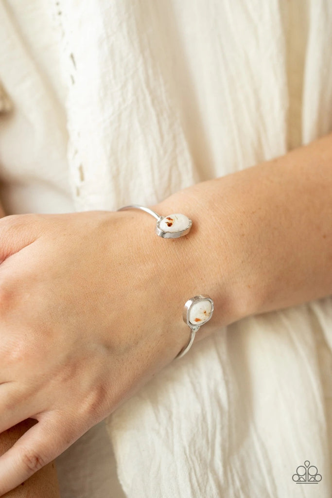 Flecks of iridescent shell-like pieces are encased inside two mismatched glassy white beads at both ends of a dainty silver open-faced cuff. The shimmery beads are encased in imperfectly hammered silver frames, adding a whimsy finish to the bubbly display.  Sold as one individual bracelet.