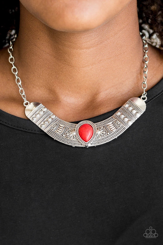 Embossed in floral and tribal inspired patterns, a shimmery silver crescent shaped frame swings below the collar in a fierce fashion. Chiseled into a tranquil teardrop, a fiery red stone is pressed into the center of the dramatic pendant for a seasonal finish. Features an adjustable clasp closure.  Sold as one individual necklace. Includes one pair of matching earrings.