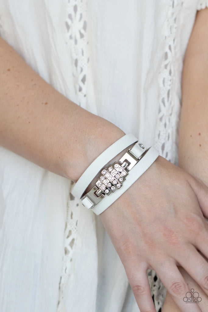 A white rhinestone silver centerpiece is studded in place by white rhinestone encrusted silver studs across the spliced center of a white leather band, creating a glittery urban look around the wrist. Features an adjustable snap closure.  Sold as one individual bracelet.