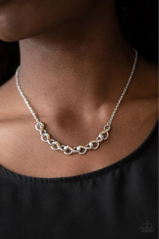 Encrusted in sections of golden topaz rhinestones, shimmery silver infinity frames delicately link below the collar for a timeless look. Features an adjustable clasp closure.  Sold as one individual necklace. Includes one pair of matching earrings.