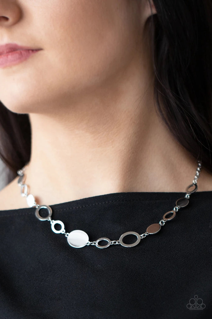 A shiny series of glistening silver discs and oval frames delicately link below the collar, creating a casual statement. Features an adjustable clasp closure.  Sold as one individual necklace. Includes one pair of matching earrings.