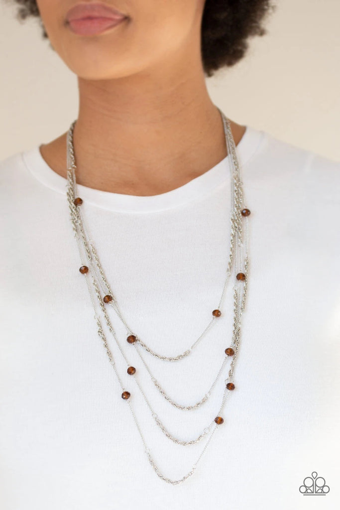 Brown crystal-like beads trickle along three mismatched silver chains, creating shimmery layers across the chest. Features an adjustable clasp closure.  Sold as one individual necklace. Includes one pair of matching earrings.