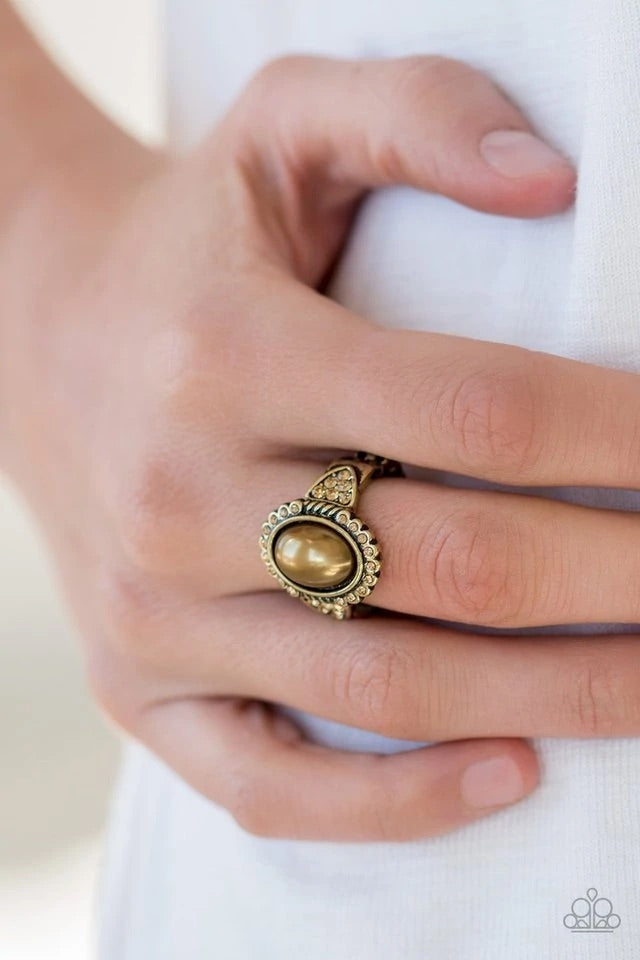 A pearly brass bead is pressed into the center of an ornate brass frame radiating with golden topaz rhinestones for a refined look. Features a stretchy band for a flexible fit. Sold as one individual ring.