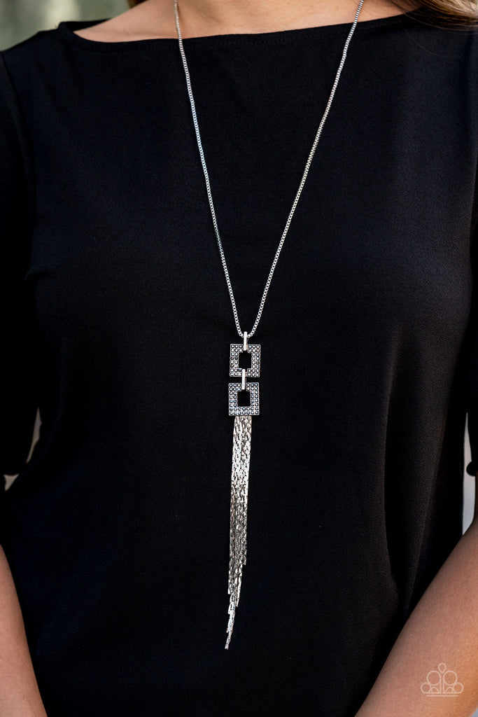 Encrusted in smoky hematite rhinestones, two squared, silver frames link at the bottom of a lengthened silver box chain. Flattened silver chains stream from the bottom of the stacked pendant, creating an edgy tassel. Features an adjustable clasp closure.  Sold as one individual necklace. Includes one pair of matching earrings.