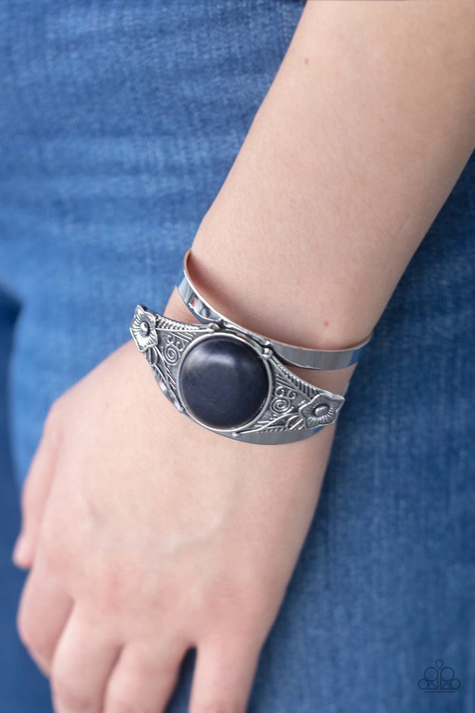A round black stone is pressed into the center of a silver frame etched and embossed in whimsical floral detail, creating a seasonal centerpiece atop a thick silver cuff.  Sold as one individual bracelet.