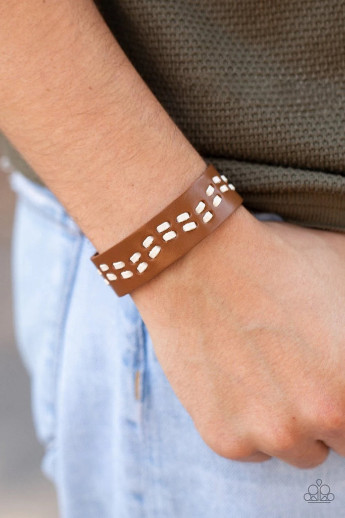 White leather cording is haphazardly laced through the center of a brown leather band, creating a rustic look around the wrist. Features an adjustable snap closure.  Sold as one individual bracelet.