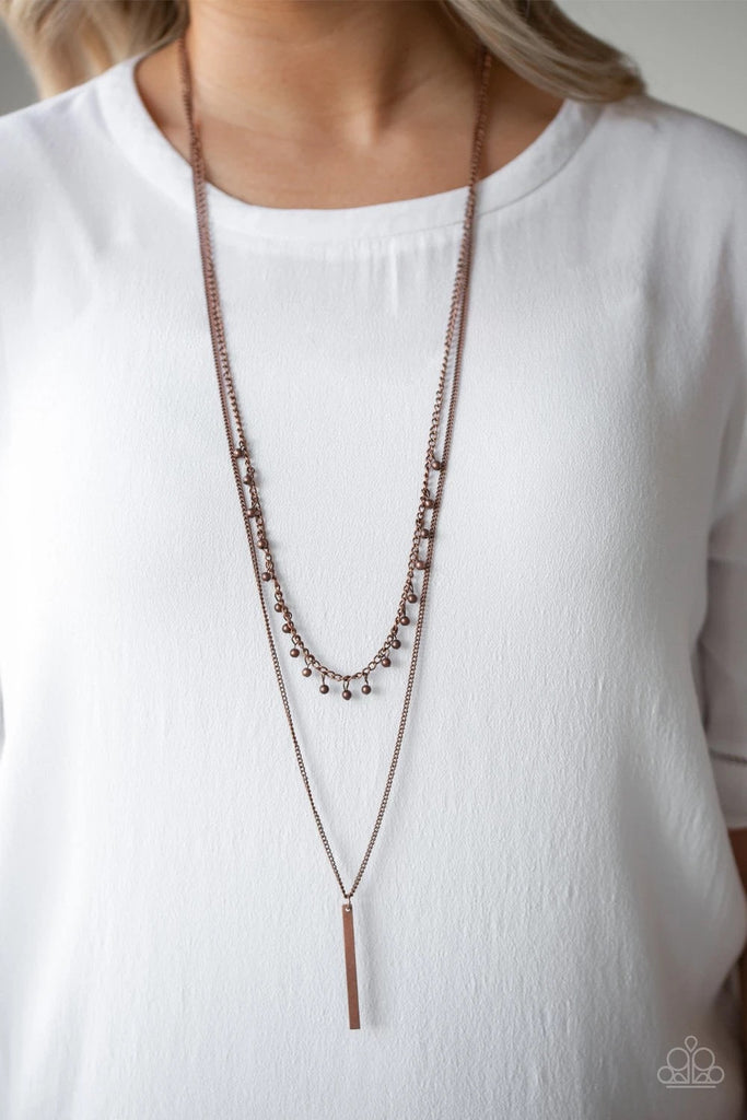 Two mismatched copper chains layer down the chest. Dainty copper beads dangle from the bottom of the uppermost chain, while a rectangular pendulum-like pendant swings from the lowermost chain for a causal finish. Features an adjustable clasp closure.  Sold as one individual necklace. Includes one pair of matching earrings.