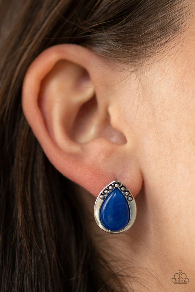 A teardrop blue stone is pressed into a studded silver frame for a whimsical look. Earring attaches to a standard post fitting.  Sold as one pair of post earrings.  