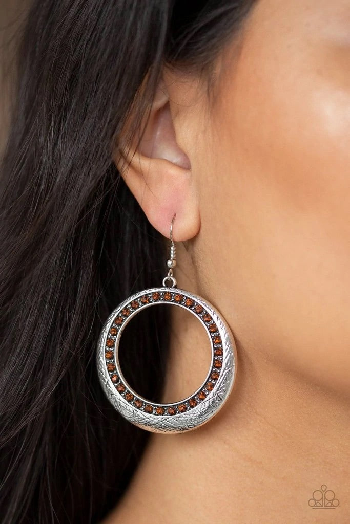 Delicately scratched in antiqued shimmer, a glistening silver hoop is encrusted in a ring of glittery topaz rhinestones for a refined look. Earring attaches to a standard fishhook fitting.  Sold as one pair of earrings.