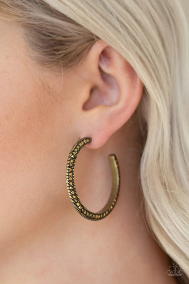 Both sides of a studded brass hoop are encrusted in golden aurum rhinestones for an edgy dazzle. Earring attaches to a standard post fitting. Hoop measures 1 1/2" in diameter. Sold as one pair of hoop earrings.