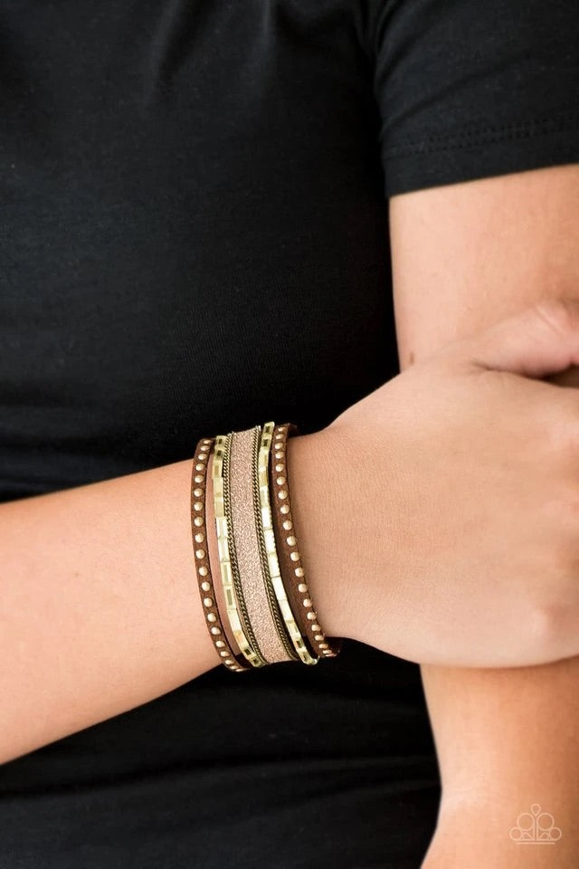 Shimmery brass studs, dainty brass chains, and golden emerald style cut rhinestones are encrusted along a brown suede band dusted in a sparkling center for a sassy look. Features an adjustable snap closure. Sold as one individual bracelet.