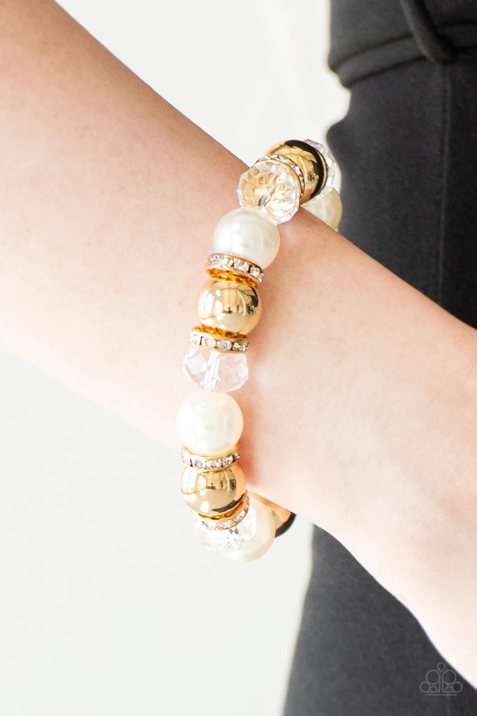 Oversized gold, crystal-like, and pearly white beads are threaded along a stretchy elastic band and wrapped around the wrist for a glamorous look. White rhinestone encrusted rings are sprinkled between the dramatic beads for a sparkling finish.  Sold as one individual bracelet.