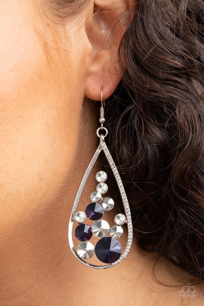 An oversized collection of glittery purple, white, and smoky rhinestones collect inside a shimmery silver teardrop. One side of the frame is encrusted in dainty white rhinestones, adding an elegant edge to the glamorous lure. Earring attaches to a standard fishhook fitting.  Sold as one pair of earrings.