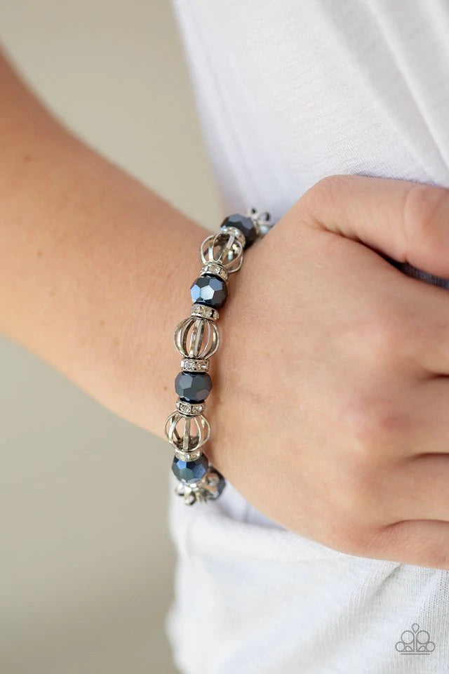 A collection of airy silver beads, faceted blue metallic beads, and white rhinestone encrusted rings are threaded along a stretchy band around the wrist for a glamorous look. Sold as one individual bracelet.