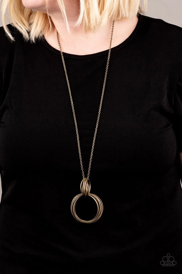 A collection of large and small antiqued brass rings interlock into a bold pendant at the bottom of a lengthened brass chain. Features an adjustable clasp closure.  Sold as one individual necklace. Includes one pair of matching earrings.