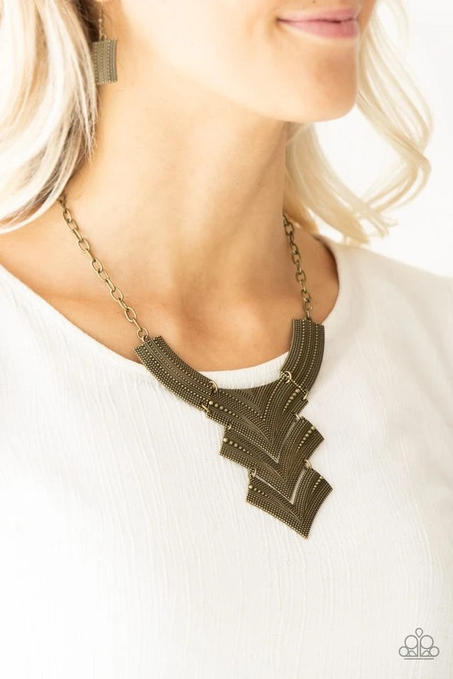 Radiating in studded details, antiqued brass plates link below the collar, joining into a fierce geometric pendant. Features an adjustable clasp closure. Sold as one individual necklace. Includes one pair of matching earrings.