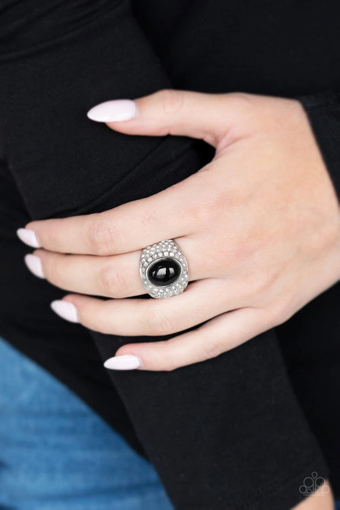 A shiny black bead is pressed into the center of a bold silver band radiating with countless white rhinestones, creating a dramatic statement piece atop the finger. Features a stretchy band for a flexible fit.  Sold as one individual ring.