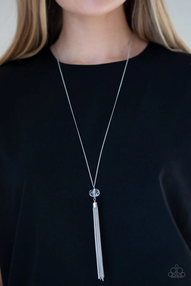 A glittery white crystal-like bead swings from the bottom of a lengthened silver chain, giving way to a shimmering silver tassel for a glamorous finish. Features an adjustable clasp closure. Sold as one individual necklace. Includes one pair of matching earrings.