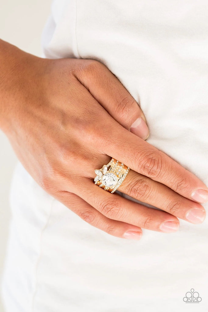 Varying in size, rows of dainty white rhinestones are encrusted along a thick gold band. Round and marquise rhinestones are pressed into the band, creating a refined centerpiece. Features a stretchy band for a flexible fit.  Sold as one individual ring.