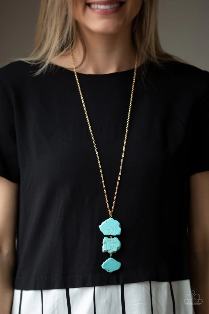 As if chipped off a cliff, pieces of turquoise rock link at the bottom of a lengthened gold chain for an earthy look. As the stone elements in this piece are natural, some color variation is normal. Features an adjustable clasp closure.  Sold as one individual necklace. Includes one pair of matching earrings.