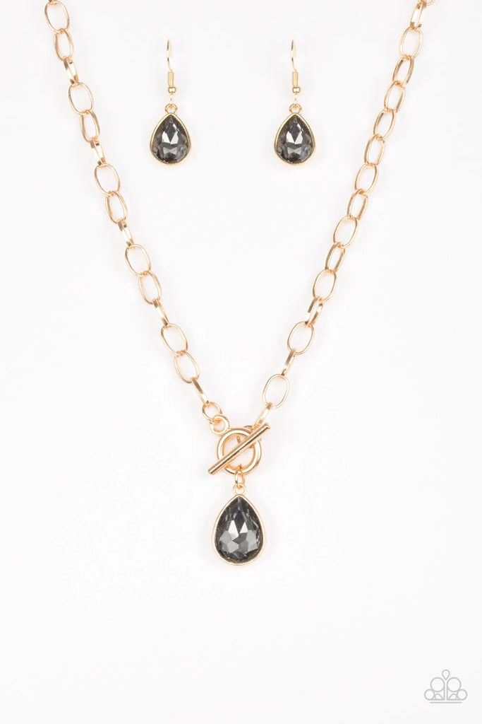 A smoky teardrop gem swings from the bottom of a shimmery gold chain, creating a classic pendant below the collar. Features a toggle closure.  Sold as one individual necklace. Includes one pair of matching earrings.