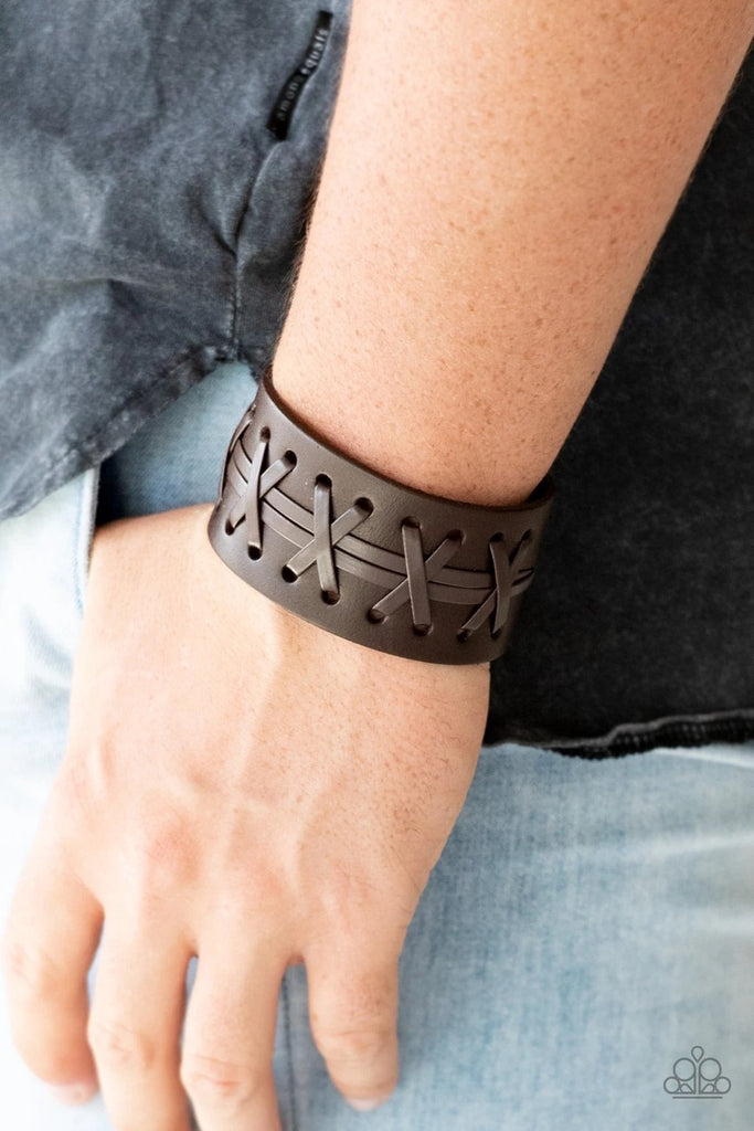 Brown leather cording is laced across the front of a thick leather band for a rugged look. Features an adjustable snap closure.  Sold as one individual bracelet.