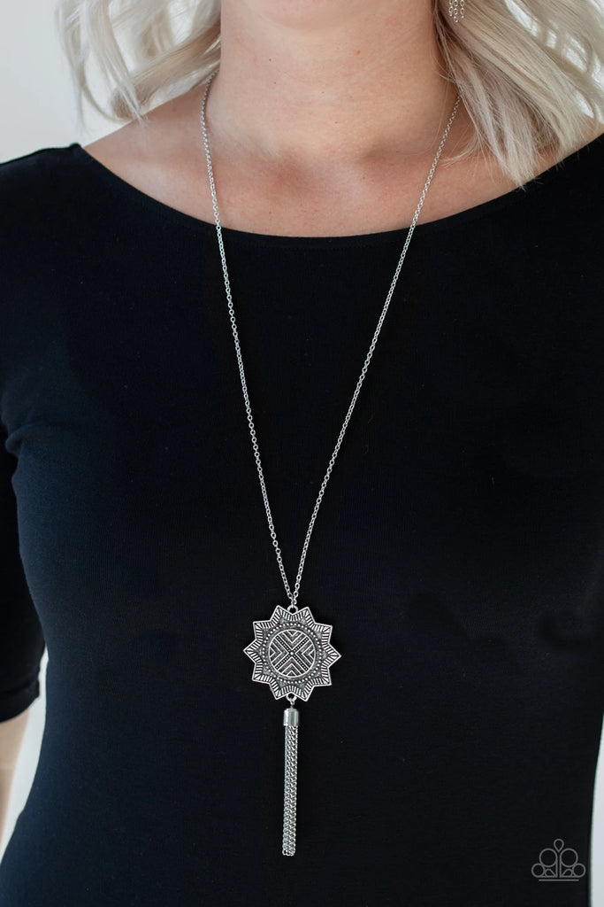 A textured sunburst pendant swings from the bottom of a lengthened silver chain. A shimmery silver chain tassel swings from the bottom of the tribal inspired pendant for a seasonal finish. Features an adjustable clasp closure.  Sold as one individual necklace. Includes one pair of matching earrings.