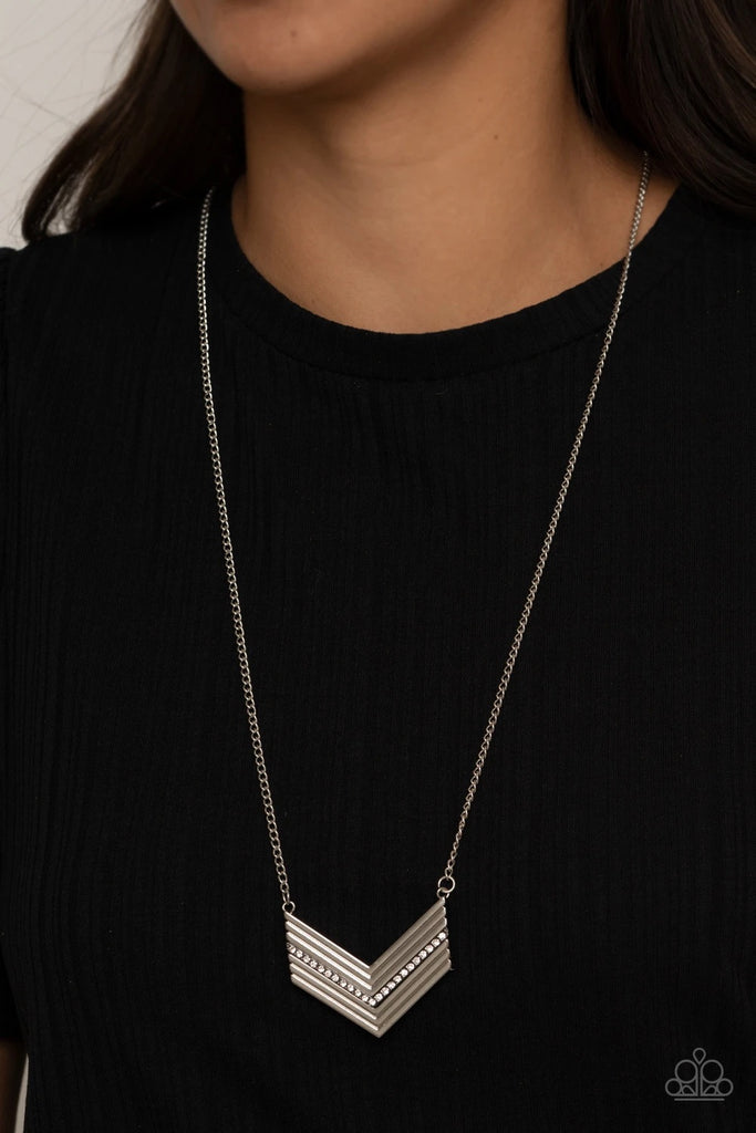 Ribbed in linear texture, the center of a stacked silver chevron-like pendant is encrusted in a row of white rhinestones for a glitzy finish. Features an adjustable clasp closure.  Sold as one individual necklace. Includes one pair of matching earrings.