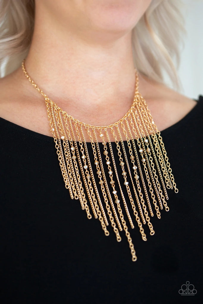 Varying in length, mismatched gold chains stream from the bottom of a classic gold chain. Faceted golden crystal-like beads sporadically dot the free-falling chains, creating a statement-making fringe below the collar. Features an adjustable clasp closure.  Sold as one individual necklace. Includes one pair of matching earrings.