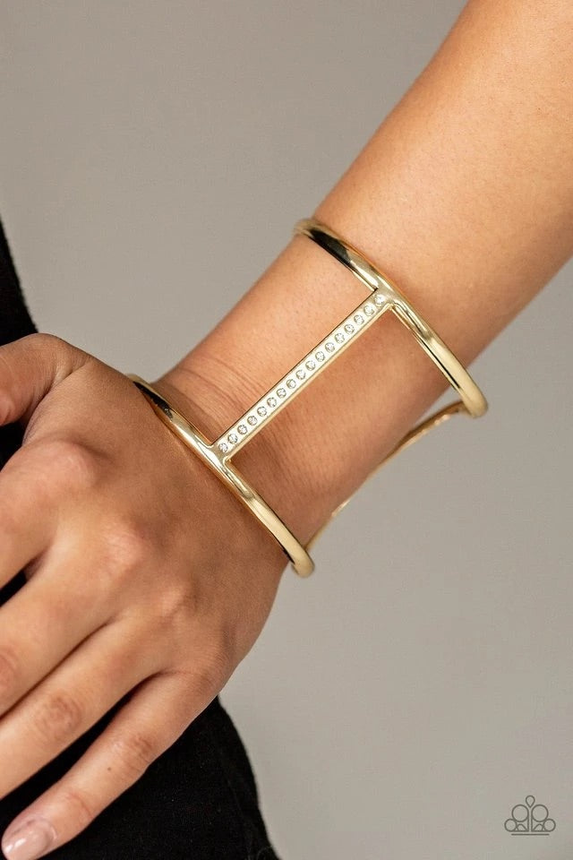 Glassy white rhinestones are encrusted down the spine of an airy gold cuff for an edgy look. Sold as one individual bracelet.