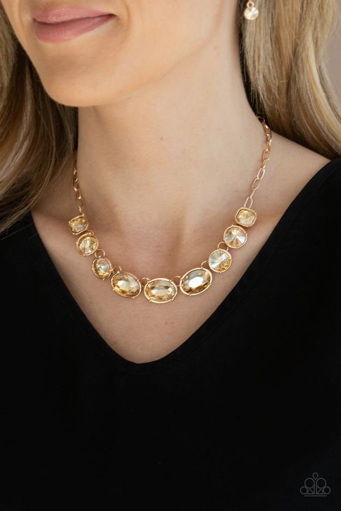 Featuring mismatched round, oval, and square cuts, a golden row of dramatically oversized rhinestones delicately link below the collar for an icy finish. Features an adjustable clasp closure.  Sold as one individual necklace. Includes one pair of matching earrings.