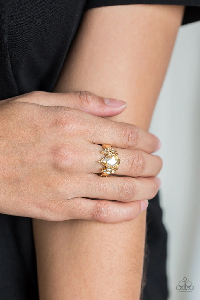 A dramatic golden teardrop gem is pressed into the center of a dainty gold band. Featuring regal marquise-cuts, dainty golden rhinestones flank the sparkling teardrop center for a glamorous finish. Features a dainty stretchy band.  Sold as one individual ring.