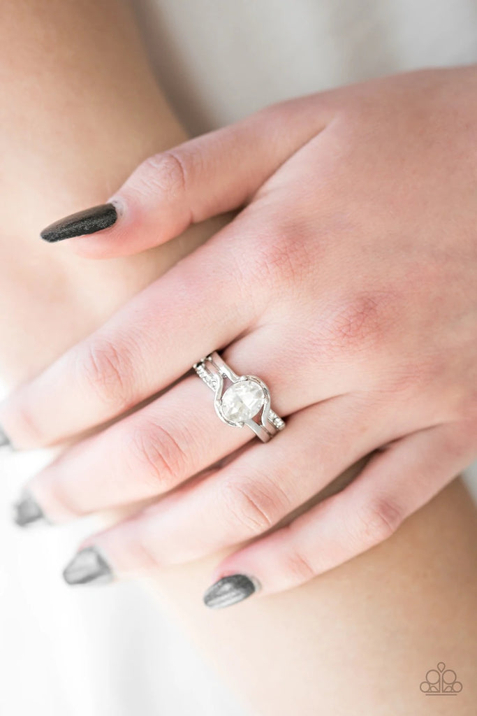 Glistening silver bands fold around a glittery white gem, creating a regal centerpiece. Sections of dainty white rhinestones encrust the outer-bands for a timeless finish. Features a dainty stretchy band for a flexible fit.  Sold as one individual ring.