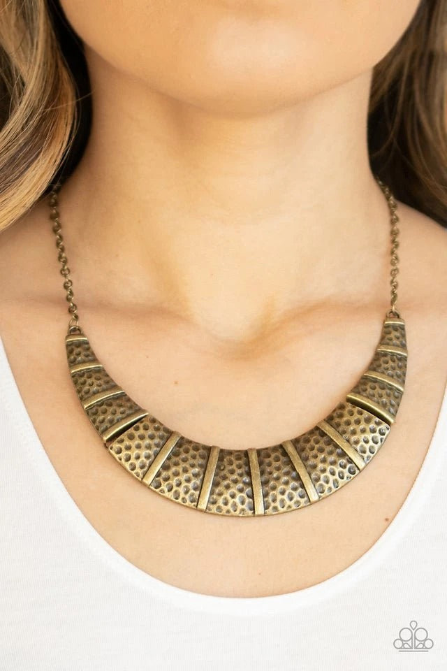 Brushed in an antiqued finish, hammered brass plates link below the collar, creating a bold crescent pendant for a statement-making look. Features an adjustable clasp closure. Sold as one individual necklace. Includes one pair of matching earrings.