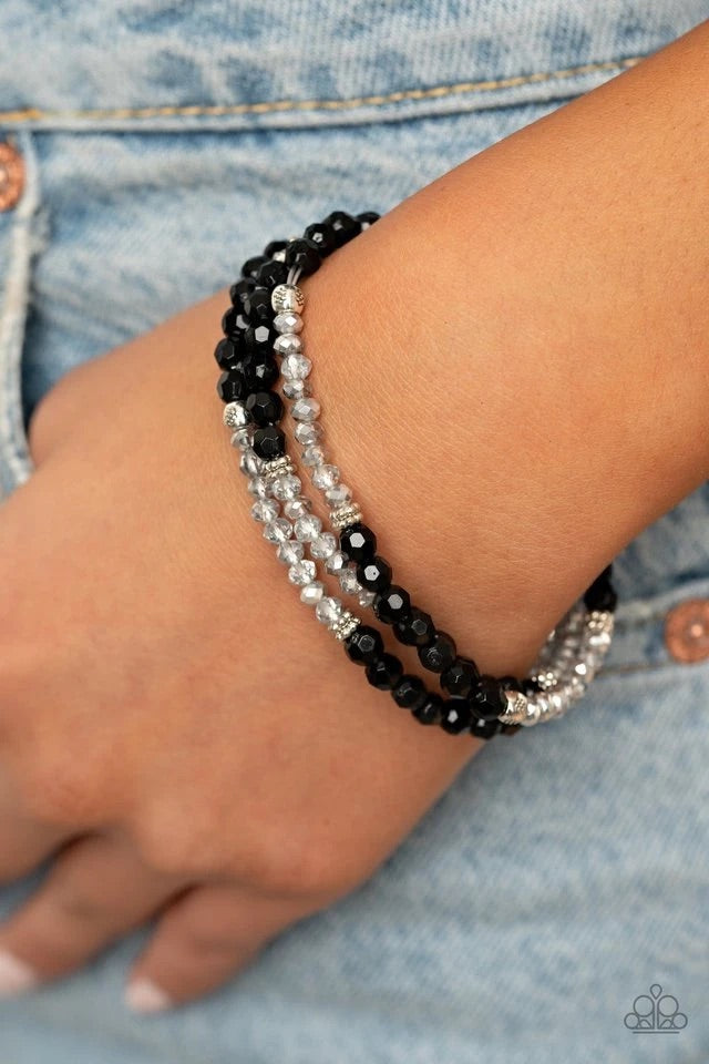 A dainty collection of glittery black and metallic flecked crystal-like beads join mismatched silver accents along stretchy bands around the wrist, creating whimsical layers.  Sold as one set of three bracelets.