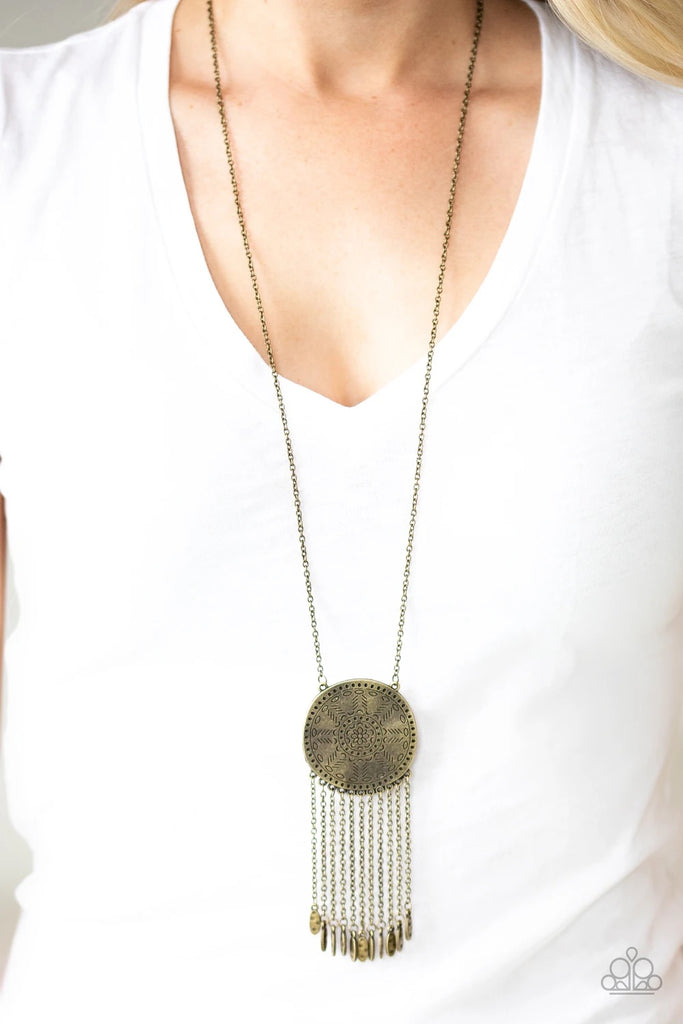 Stamped in a decorative floral pattern, an imperfect brass disc swings from the bottom of a lengthened brass chain. Brass chains and hammered brass beads stream from the bottom of the rustic pendant, creating a flirty fringe. Features an adjustable clasp closure.  Sold as one individual necklace. Includes one pair of matching earrings.