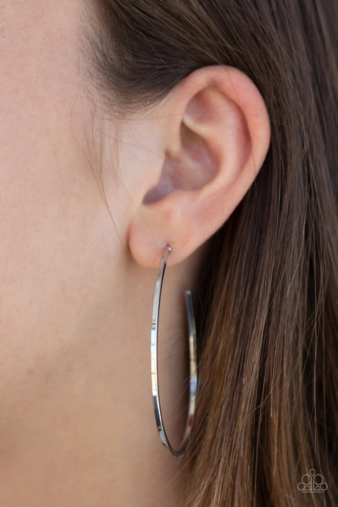 A glistening silver bar unexpectedly curls into an edgy shaped hoop for an abstract look. Earring attaches to a standard post fitting. Hoop measures approximately 1 3/4" in diameter.  Sold as one pair of hoop earrings.