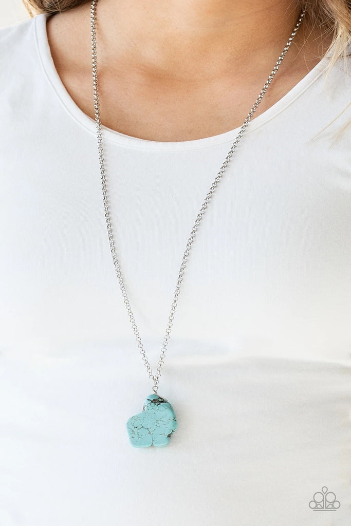 A large turquoise stone pendant hangs from a wire-wrap fitting for an artisan flair. Infused with an elongated silver chain, the earthy stone features rigid and uneven edges as if the pendant had been chipped from a cliff. As the stone elements in this piece are natural, some color variation is normal. Features an adjustable clasp closure.  Sold as one individual necklace. Includes one pair of matching earrings.