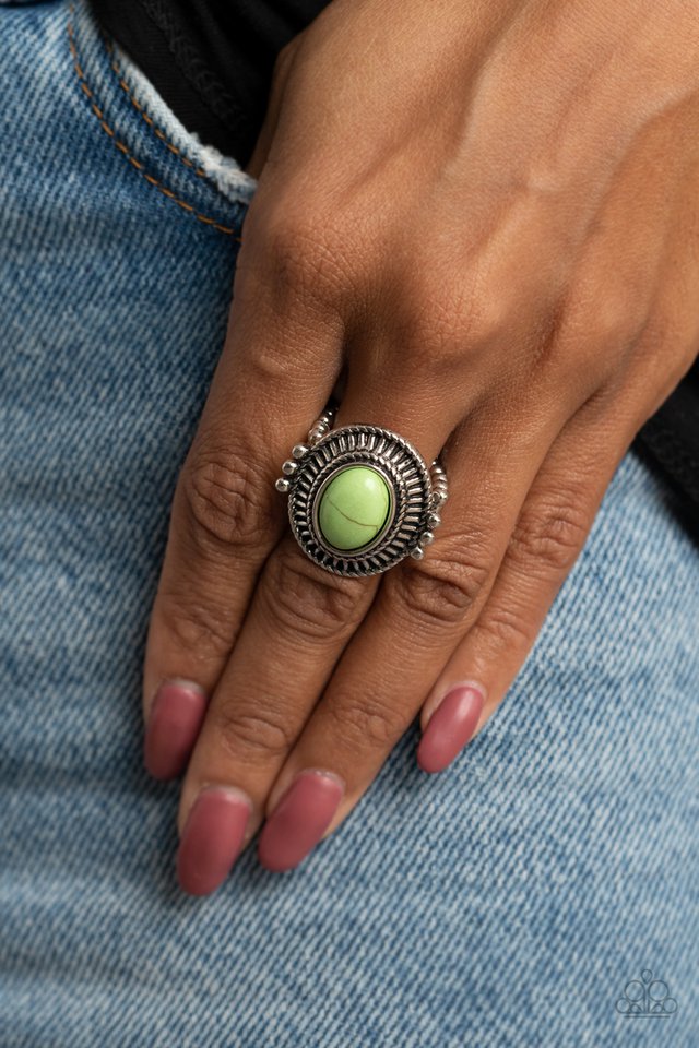 An oval green stone is pressed into the center of an antiqued silver frame radiating with striking linear texture. The colorful centerpiece is held in place with faux pronged silver studs, creating a bold tribal inspired statement. Features a stretchy band for a flexible fit.  Sold as one individual ring.