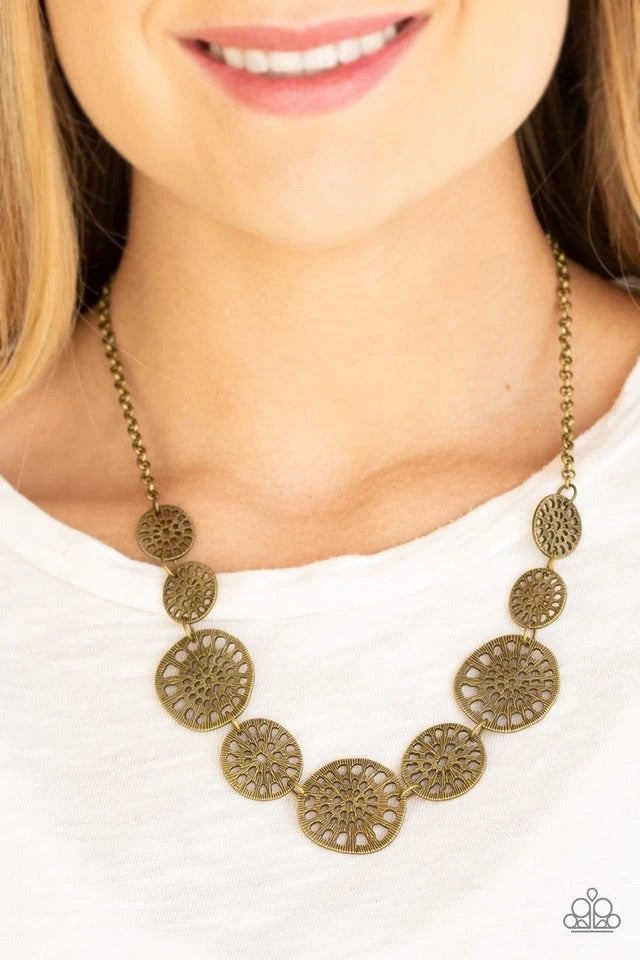 Featuring airy stenciled patterns, shimmery brass discs link below the collar for a whimsical asymmetrical look. Features an adjustable clasp closure.  Sold as one individual necklace. Includes one pair of matching earrings.