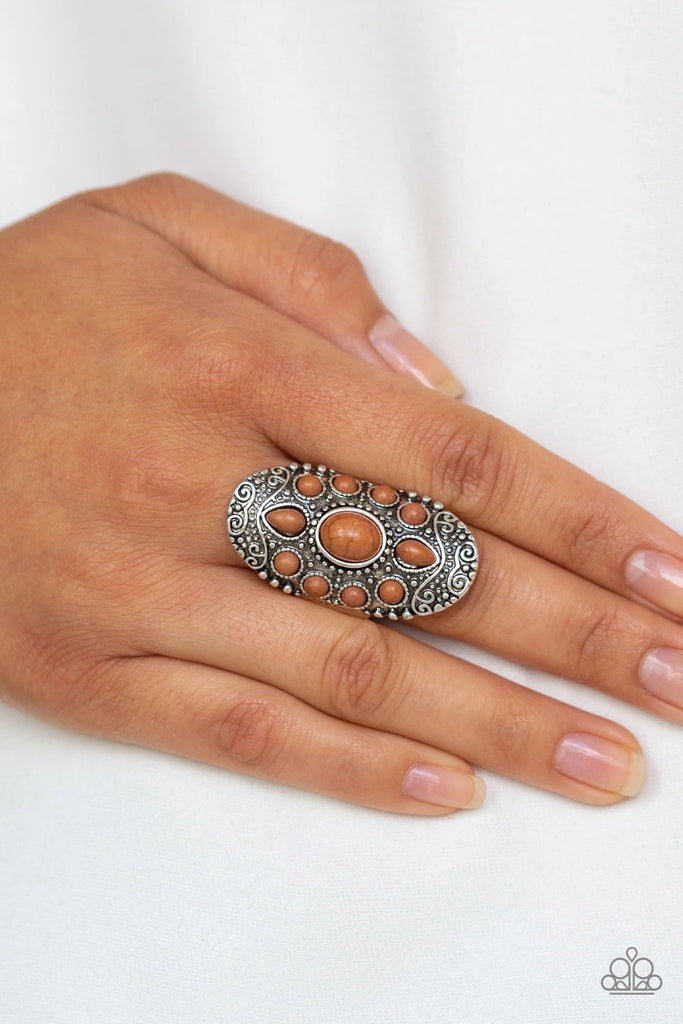 Embossed in a studded filigree pattern, an oval silver frame folds around the finger. Featuring round, oval, and teardrop shapes, earthy brown stone beads are pressed into the center of the frame, creating a whimsical floral pattern. Features a stretchy band for a flexible fit.  Sold as one individual ring.