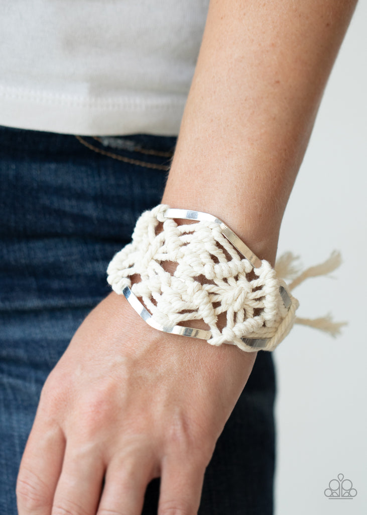 White cording decoratively knots and weaves around an airy silver cuff for a macramé inspired look. Knotted around the ends, white tassels flair out from bottoms of the cuff for a wanderlust finish. Sold as one individual cuff bracelet